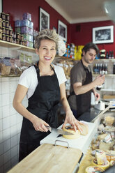 Porträt einer glücklichen Verkäuferin, die in einem Supermarkt Käse schneidet - MASF05470