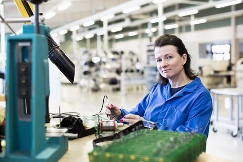 Porträt einer selbstbewussten Technikerin bei der Arbeit an einer Leiterplatte am Schreibtisch in der Industrie - MASF05472