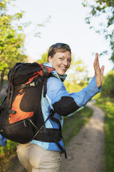Porträt eines glücklichen weiblichen Rucksacktouristen, der beim Wandern im Wald winkt - MASF05487