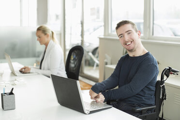 Porträt eines glücklichen Geschäftsmannes mit zerebraler Lähmung, der einen Laptop im Büro benutzt - MASF05496