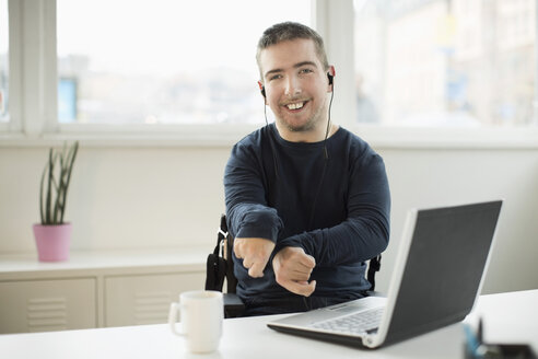 Porträt eines glücklichen behinderten Geschäftsmannes mit Laptop am Schreibtisch im Büro - MASF05497