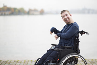 Porträt eines glücklichen Mannes mit zerebraler Lähmung, der im Rollstuhl am See sitzt - MASF05498