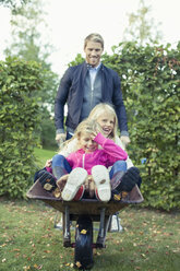 Playful father pushing daughters on wheelbarrow at yard - MASF05504