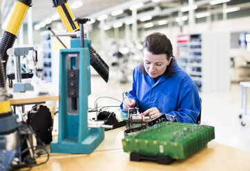 Mid adult female electrician working on circuit board at desk in industry - MASF05518