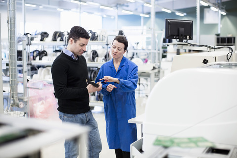 Mittlere erwachsene Technikerin, die einem Kunden in einer Fabrik ein Maschinenteil erklärt, lizenzfreies Stockfoto