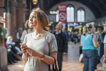 Mid adult woman with mobile phone looking up while standing on railway station - MASF05530