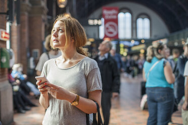Mittlere erwachsene Frau mit Mobiltelefon, die auf dem Bahnhof steht und nach oben schaut - MASF05530