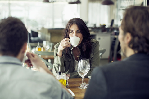 Reife Frau trinkt Kaffee, während sie einen Kollegen beim Mittagessen im Restaurant ansieht, lizenzfreies Stockfoto