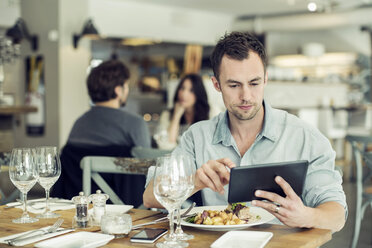 Mittlerer Erwachsener, der ein digitales Tablet benutzt, während er in einem Restaurant zu Mittag isst - MASF05543