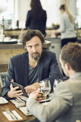 Älterer Geschäftsmann, der mit einem Kollegen am Restauranttisch über ein digitales Tablet diskutiert - MASF05569