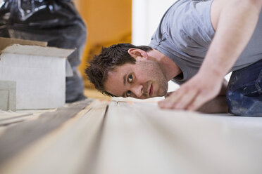 Männlicher Zimmermann bei der Kontrolle einer Holzbohle auf der Baustelle - MASF05573