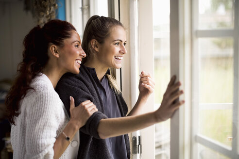 Glückliche Frauen blicken durch das Fenster auf das Sommerhaus hinaus - MASF05576