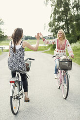 Happy female friends giving high five while cycling on country road - MASF05593