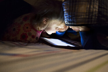 Siblings using tablet computer on bed in darkroom at home - CAVF43028