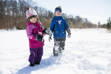 Playful siblings enjoying on snow covered field against sky - CAVF43040