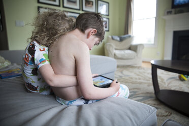 Mädchen umarmt Bruder mit Tablet-Computer auf Sofa zu Hause - CAVF43048