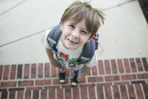 Hochformatiges Porträt eines Jungen mit Rucksack, der auf einer Treppe steht, lizenzfreies Stockfoto