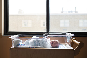 Baby boy yawning while sleeping in crib by window at hospital - CAVF43066