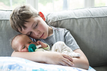 Boy embracing brother while sitting on sofa at home - CAVF43071