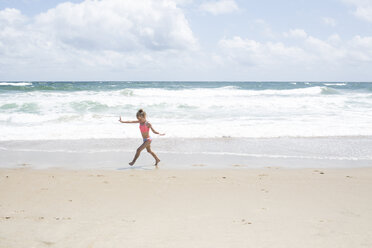 Verspieltes Mädchen läuft am Strand gegen bewölkten Himmel - CAVF43084