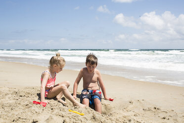 Geschwister spielen mit Sand am Strand gegen den Himmel an einem sonnigen Tag - CAVF43085