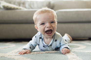 Portrait of cheerful baby boy lying on carpet at home - CAVF43092