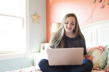 Happy woman using laptop computer on bed at home - CAVF43096