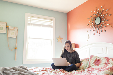 Frau benutzt einen Laptop, während sie zu Hause auf dem Bett sitzt, lizenzfreies Stockfoto