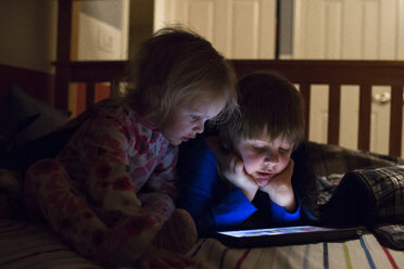 Siblings using tablet computer on bed at home - CAVF43107