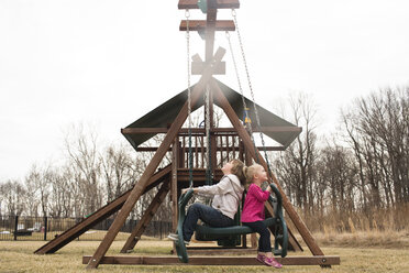 Verspielte Geschwister schaukeln auf dem Spielplatz gegen den klaren Himmel - CAVF43109