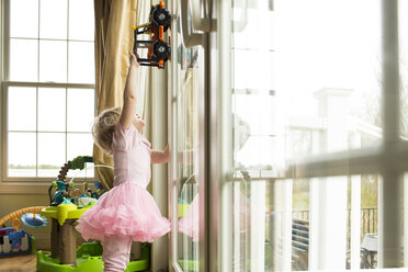 Mädchen spielt mit Spielzeugauto am Fenster zu Hause - CAVF43120