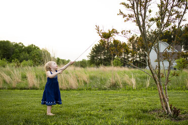 Mädchen, das mit einem Stock spielt, während es auf einem grasbewachsenen Feld vor einem klaren Himmel steht - CAVF43121