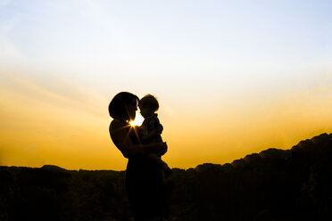 Silhouette mother carrying son while standing in park against sky during sunset - CAVF43129