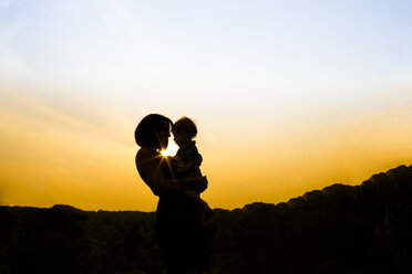 Silhouette Mutter mit Sohn im Park gegen den Himmel bei Sonnenuntergang stehend - CAVF43129