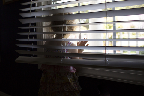 Mädchen schaut durch das Fenster, während sie zu Hause steht, lizenzfreies Stockfoto
