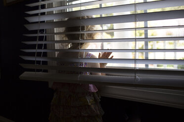 Mädchen schaut durch das Fenster, während sie zu Hause steht - CAVF43130