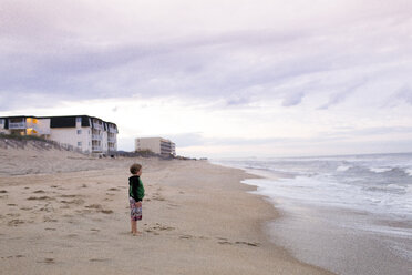 Side view of boy standing at beach against cloudy sky - CAVF43135