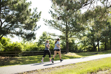 Mutter und Tochter joggen in voller Länge auf dem Fußweg im Park an einem sonnigen Tag - CAVF43141