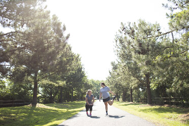 Mutter und Tochter, die sich die Beine vertreten, während sie an einem sonnigen Tag auf einem Fußweg im Park trainieren - CAVF43142