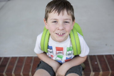 Hochformatiges Porträt eines Jungen mit Rucksack, der auf einer Veranda sitzt - CAVF43151