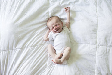 Draufsicht auf einen kleinen Jungen, der sich auf dem Bett liegend streckt - CAVF43153