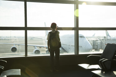 Rückansicht eines Jungen mit Rucksack, der durch das Fenster schaut, während er im Flughafen steht - CAVF43156