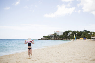 Girl holding hat while walking against sea and sky at beach - CAVF43161