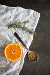 Blick von oben auf eine Orangenscheibe mit einem Löffel mit Zucker und Rosmarin auf einer Serviette - CAVF43179