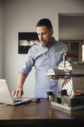 Mann mit Laptop und Kaffeeröster in einem Cafe - CAVF43189