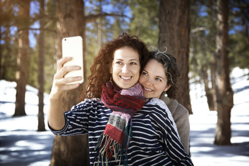 Lächelnde Freunde, die ein Selfie machen, während sie im Winter im Wald stehen - CAVF43200