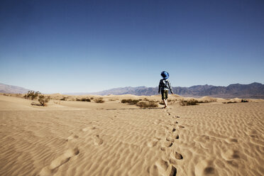 Rear view of boy walking at desert against clear blue sky - CAVF43210