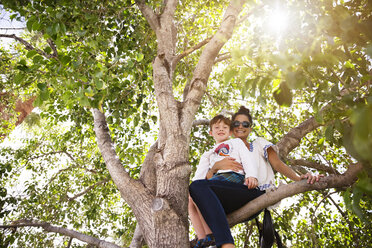 Low angle portrait of happy mother and son sitting on branch - CAVF43216