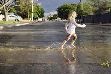 Seitenansicht eines Mädchens, das während der Regenzeit auf der nassen Straße läuft - CAVF43219