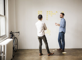 Geschäftsleute diskutieren über Haftnotizen an einer weißen Wand im Kreativbüro - CAVF43249